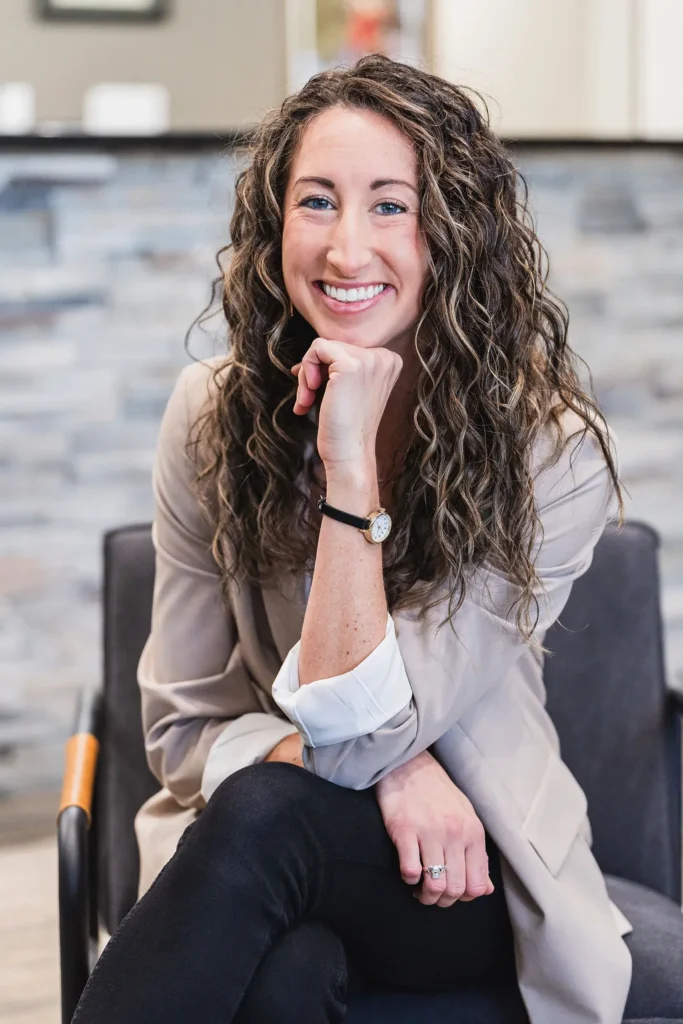 Dr. Sara Cahill smiling looking professional sitting down while hand is on her chin in front of reception area at Wayson Family Chiropractic