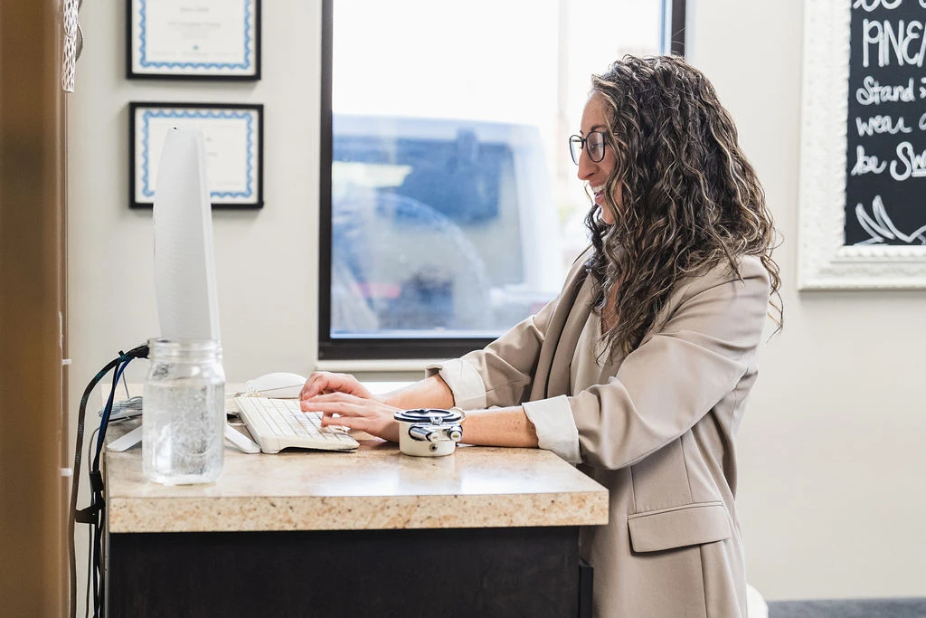 Dr. Sara Cahill standing behind desk typing while smiling
