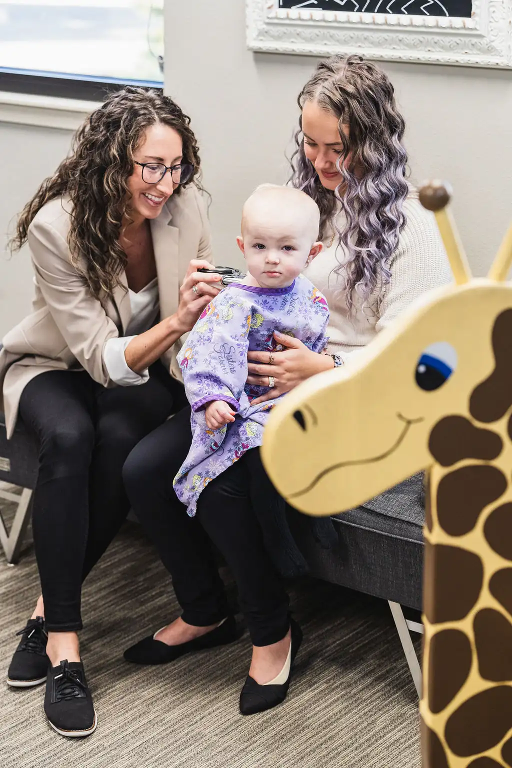 Dr. Sara Cahill performing a spinal adjustment for baby while she sits up and mother is holding her for comfort