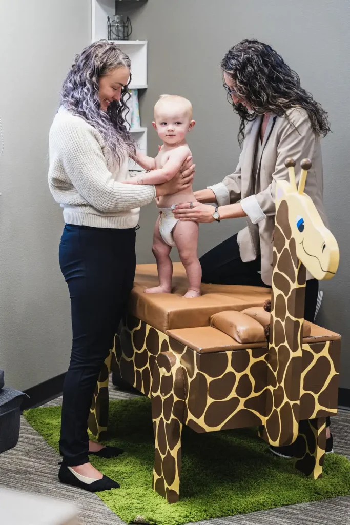 Baby standing on fun giraffe chiropractic adjustment table being checked by Dr. Sara Cahill