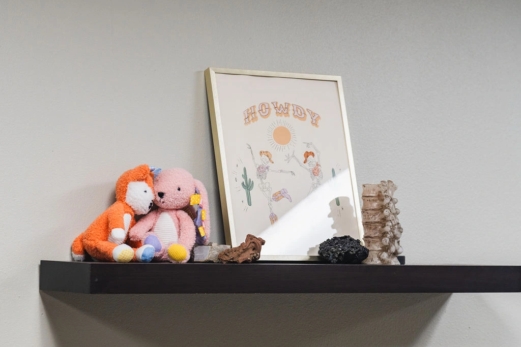 Stuffed animals and a picture that reads "howdy" on a shelf