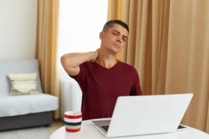 Man working on laptop at home rubbing his neck from strain and stiffness