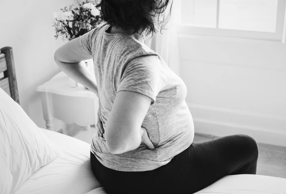 Pregnant woman sitting on bed holding lower back due to pain