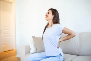 Woman sitting on couch experiencing persistent lower back pain