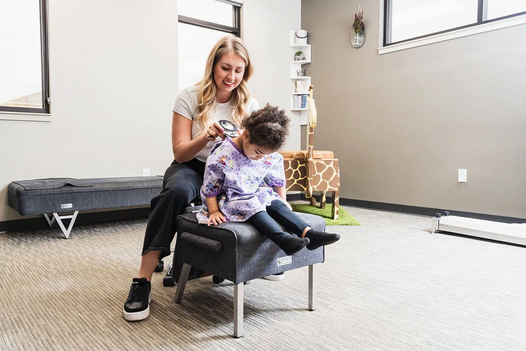 A woman examines a young child's back with a device in a clinic setting.