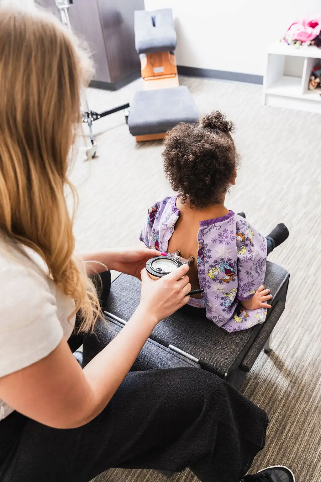 A woman uses a medical device on a young child's exposed back.